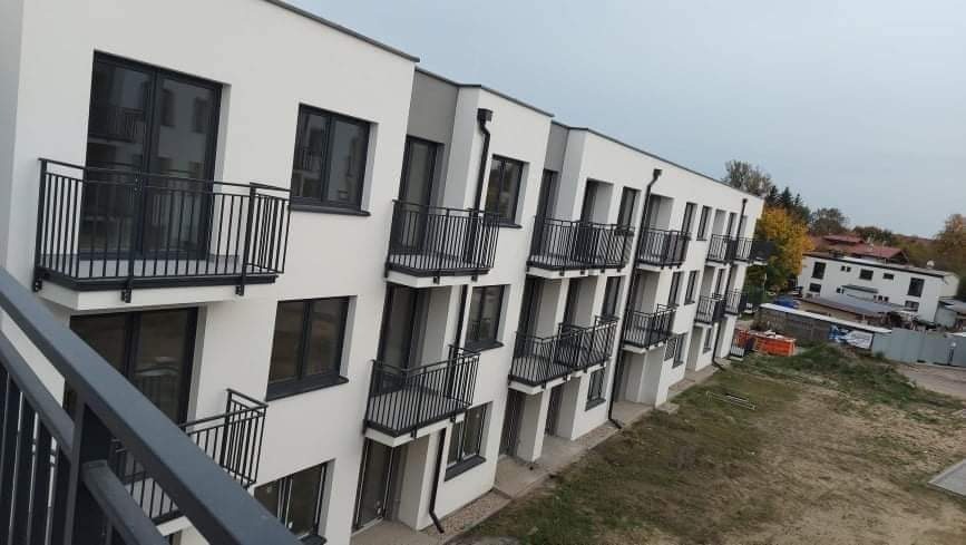 Nowy, wielopiętrowy budynek mieszkalny z czarnymi balkonami w Serocku, widok z góry, z widocznymi elementami krajobrazu w tle.