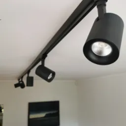 Czarny system szynowy z reflektorami LED zamontowany na suficie, oświetlający wnętrze z obrazem na ścianie w tle.