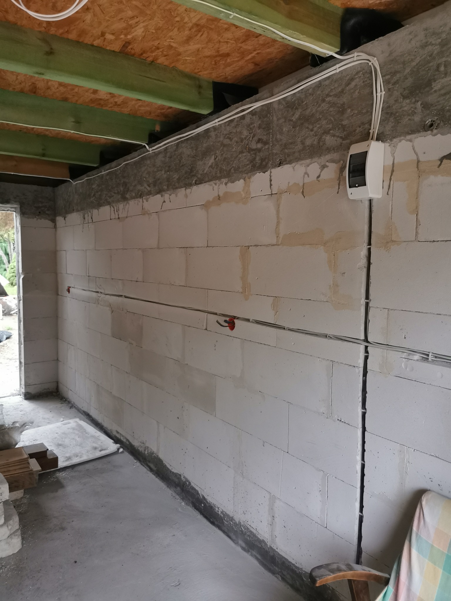 Wewnętrzna ściana budynku w trakcie prac instalacyjnych, widoczne kable elektryczne prowadzone po ścianie i pod sufitem oraz skrzynka rozdzielcza zamontowana na ścianie.