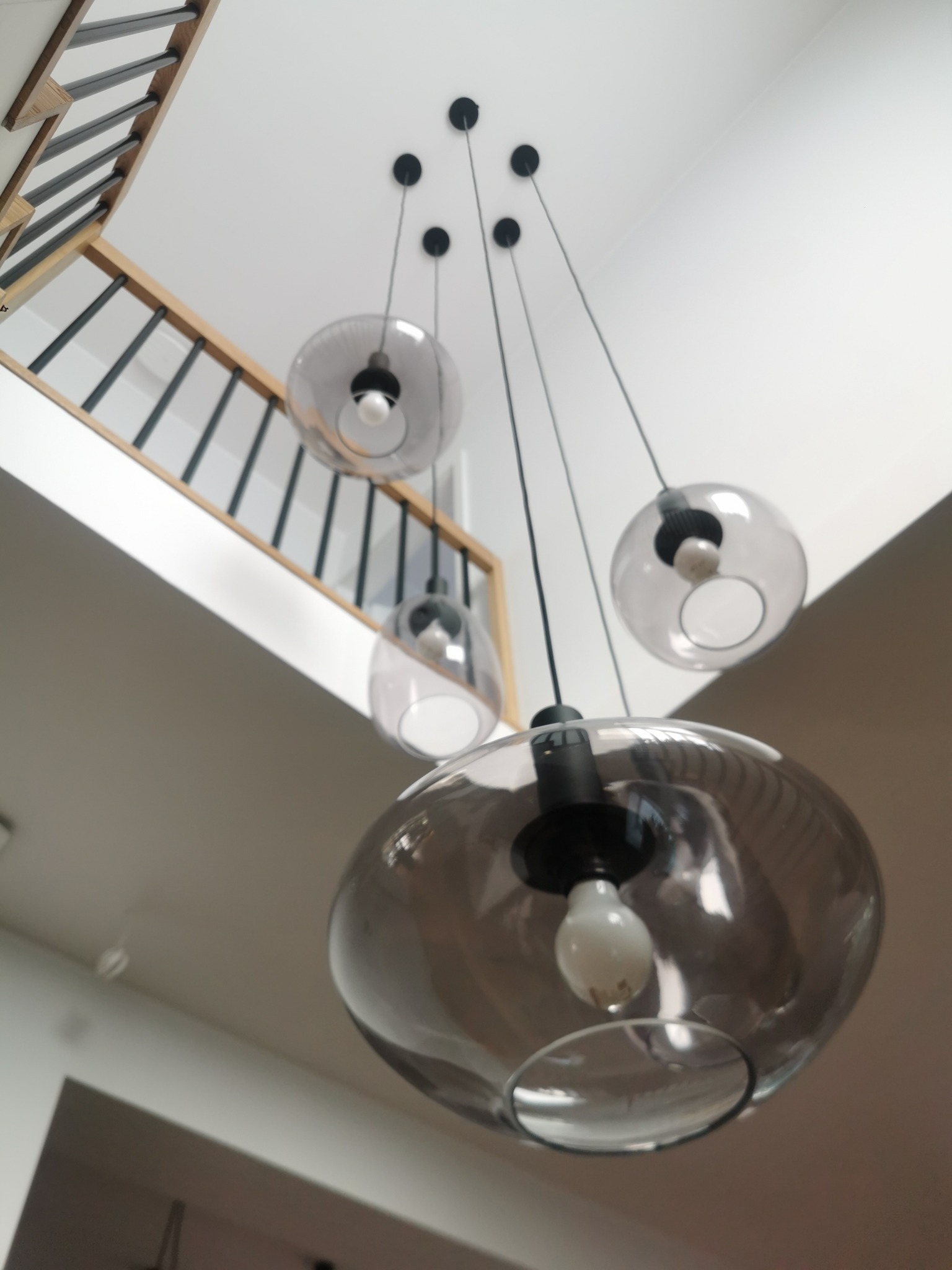 Zawieszone szklane lampy kuliste z widoczną konstrukcją schodów w tle.
