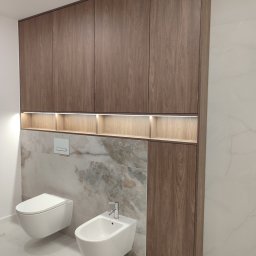 Paweł Kmieć Meble przy lesie - Nowoczesna zabudowa łazienkowa z szafkami z drewna orzechowego, podświetlanymi półkami i marmurowym panelem nad toaletą i bidetem. Minimalistyczny design.