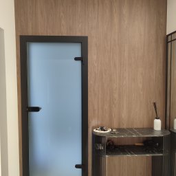 Paweł Kmieć Meble przy lesie - Nowoczesne wnętrze: drewniana boazeria, szklane drzwi w czarnej ramie i konsola z marmurowym blatem. Minimalistyczny design, eleganckie wykończenie.