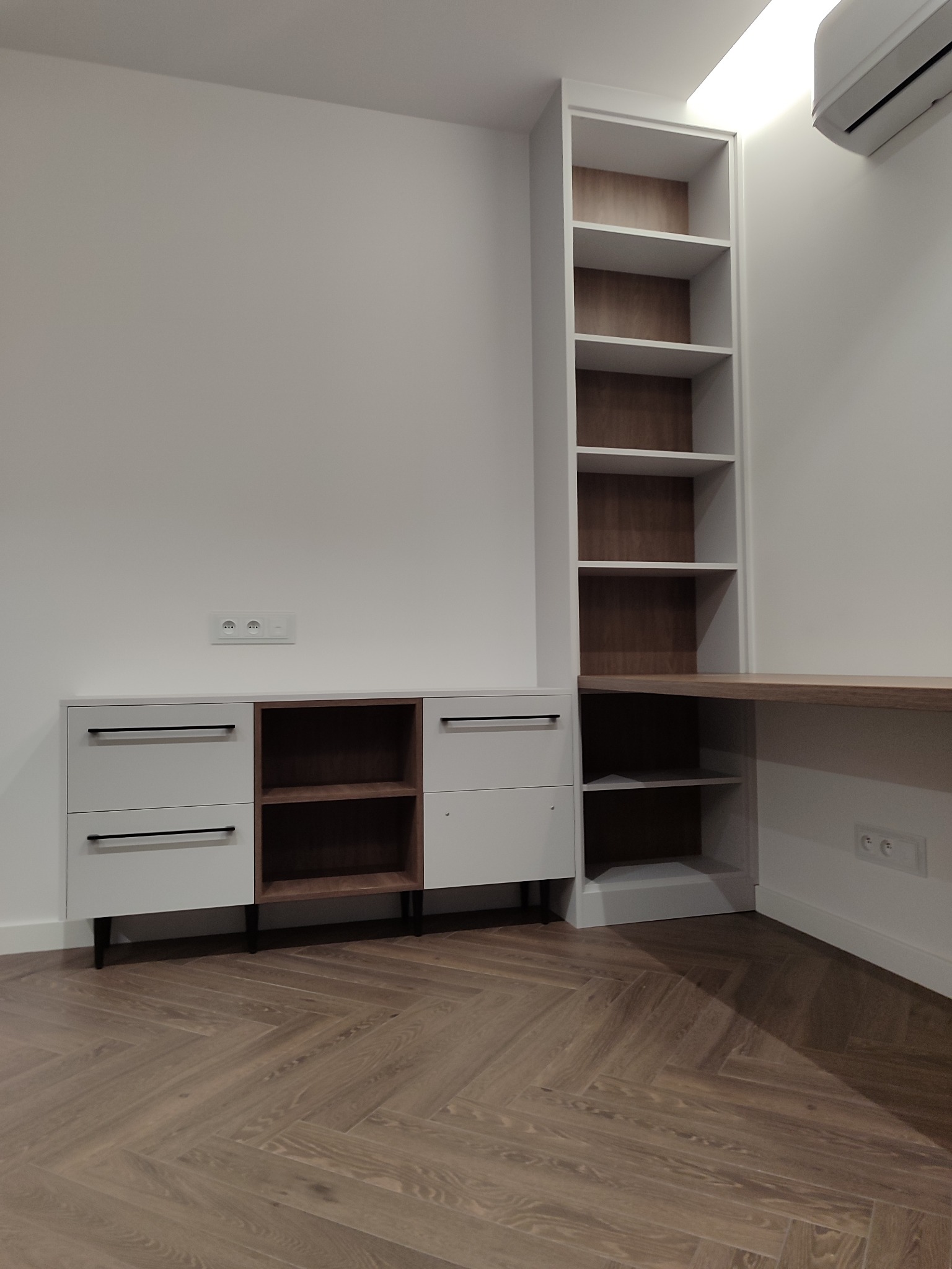 Biało-brązowy zestaw mebli na wymiar: szafka z szufladami i otwartymi półkami, wysoki regał z biurkiem, parkiet w jodełkę. Minimalistyczny design, nowoczesne wykończenie.