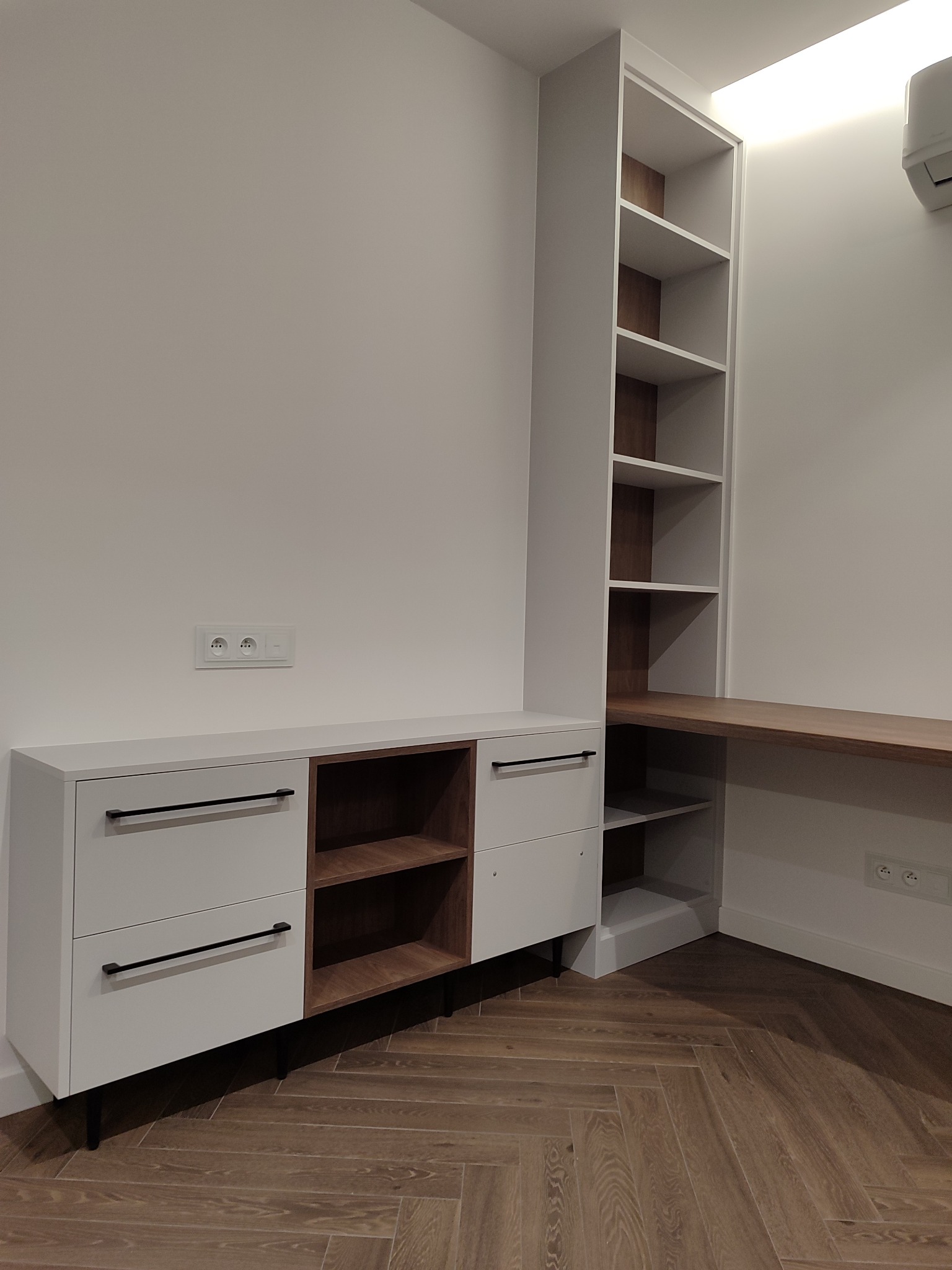 Biało-drewniana zabudowa meblowa z biurkiem i szafkami w stylu minimalistycznym, widok na parkiet w jodełkę. Realizacja z Lublina.