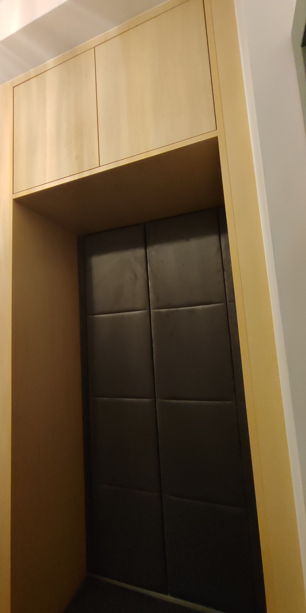 Wnęka z przesuwnymi, ciemnymi drzwiami i jasną zabudową meblową u góry. Minimalistyczny design, pionowy kadr.