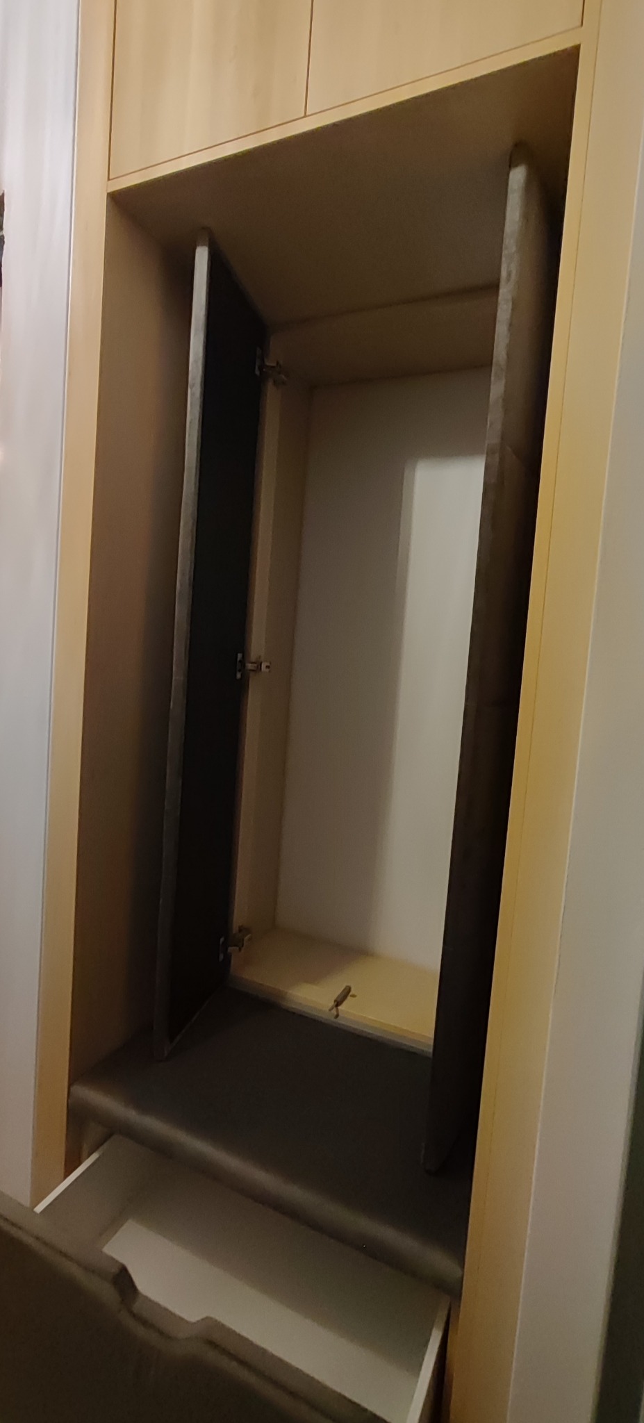 Otwarta szafka wnękowa z szufladą, widoczne zawiasy i półki. Jasne drewno, minimalistyczny design. Ujęcie z bliska, wnętrze szafki białe.