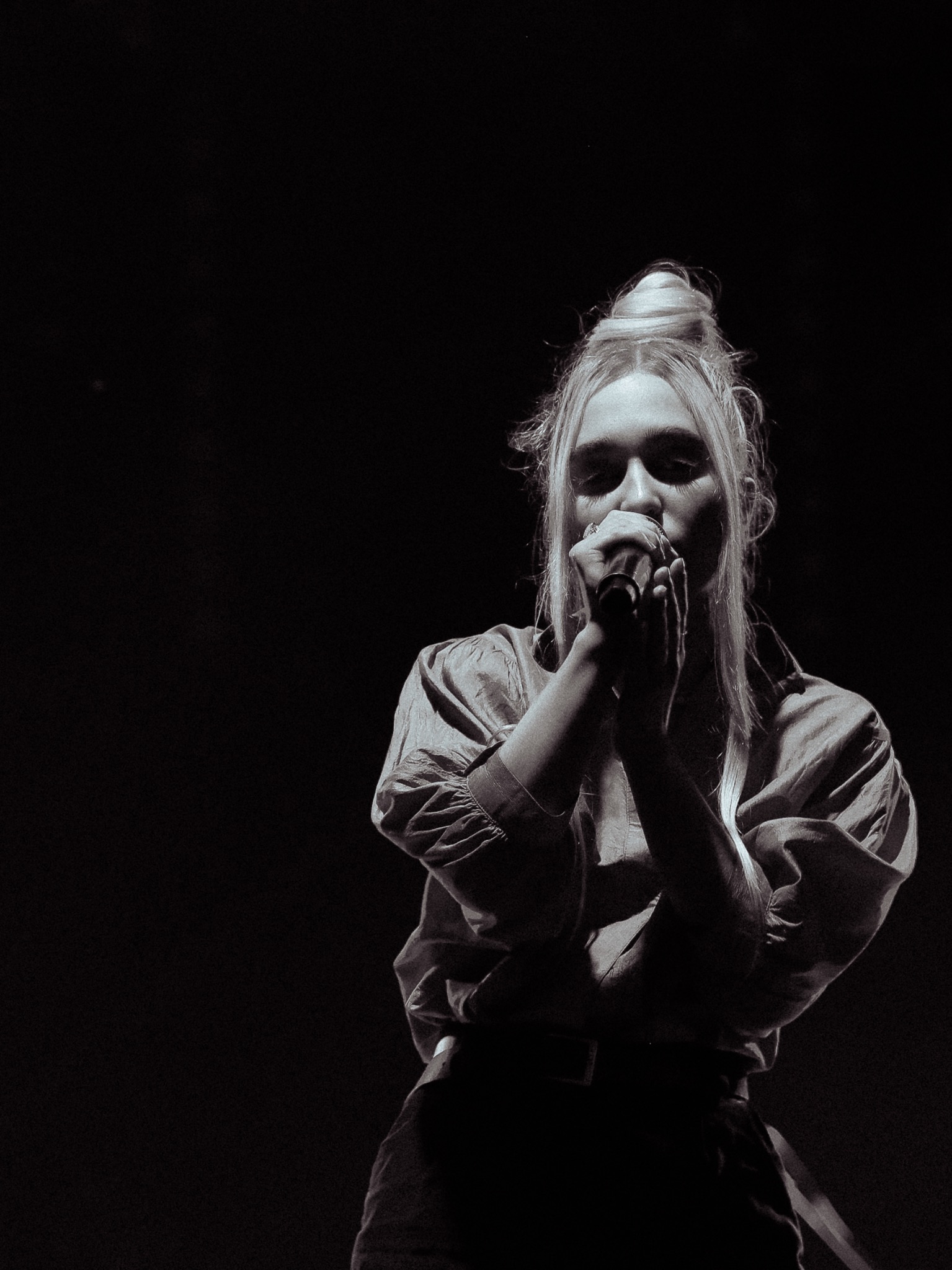 Czarno-białe zdjęcie piosenkarki z wysoko upiętymi włosami, śpiewającej do mikrofonu podczas występu na scenie.