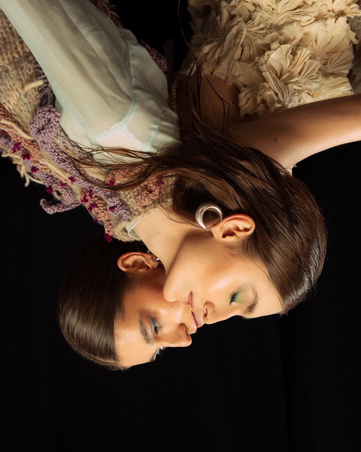 Portret kobiety z mokrymi włosami, w pastelowej sukience i z dużym srebrnym kolczykiem, na czarnym tle, z delikatnym makijażem w odcieniach zieleni.