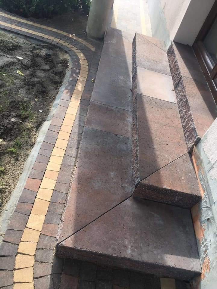 Schody wejściowe i chodnik wyłożone kostką brukową w odcieniach brązu i beżu, z widoczną kolumną i fragmentem elewacji budynku.