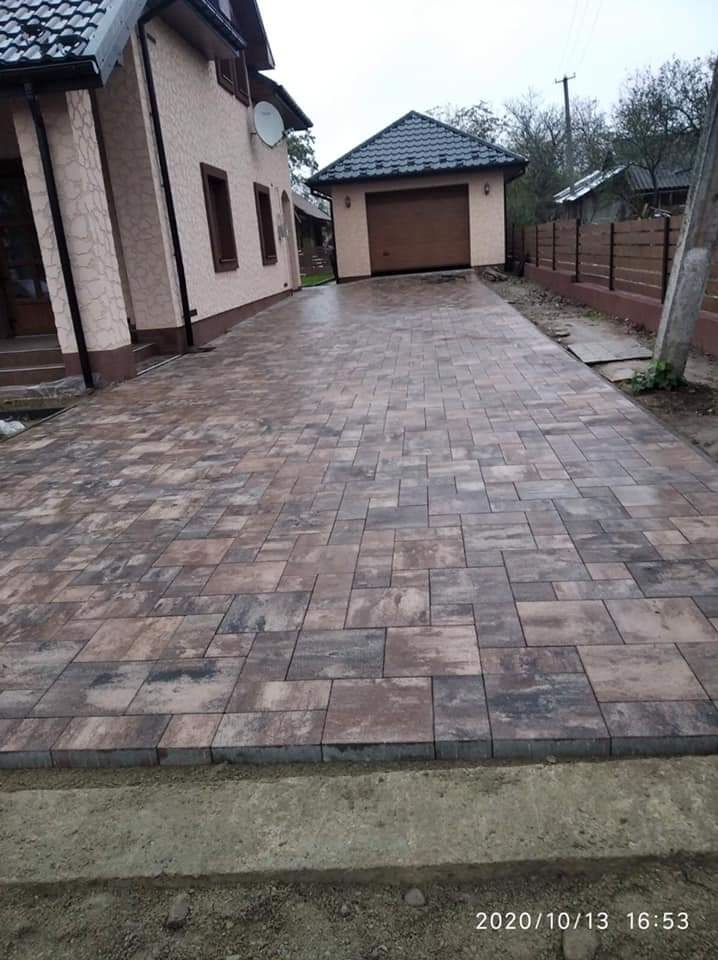 Ułożona kostka brukowa prowadząca od domu do garażu, widoczne różnokolorowe prostokątne elementy tworzące wzór, świeżo ułożona, z pozostawionym miejscem na obrzeża.