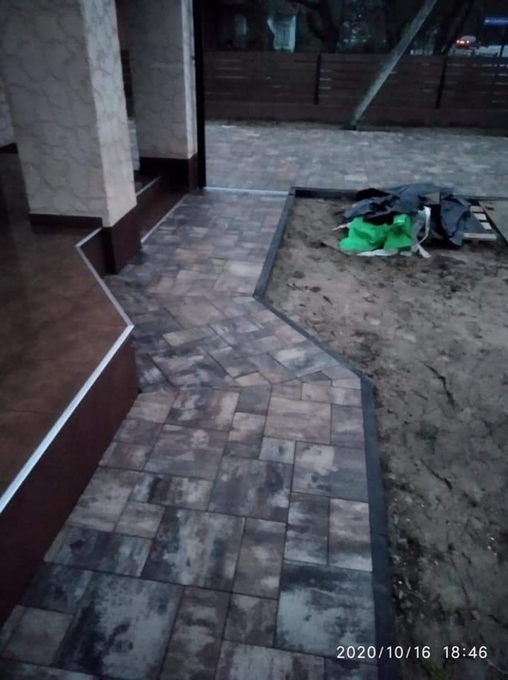 Ułożona ścieżka z kostki brukowej prowadząca do domu w Łomiankach, widoczne pozostałości po pracach ziemnych obok ścieżki.