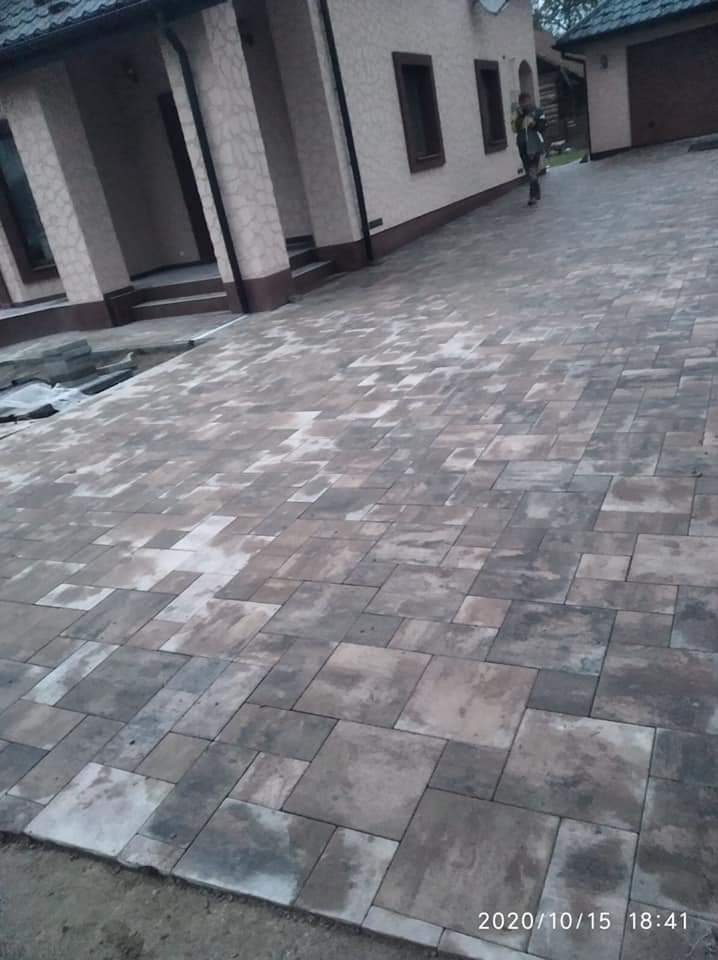 Ułożona kostka brukowa w odcieniach szarości i brązu przed budynkiem z kolumnami, widoczna osoba w tle.