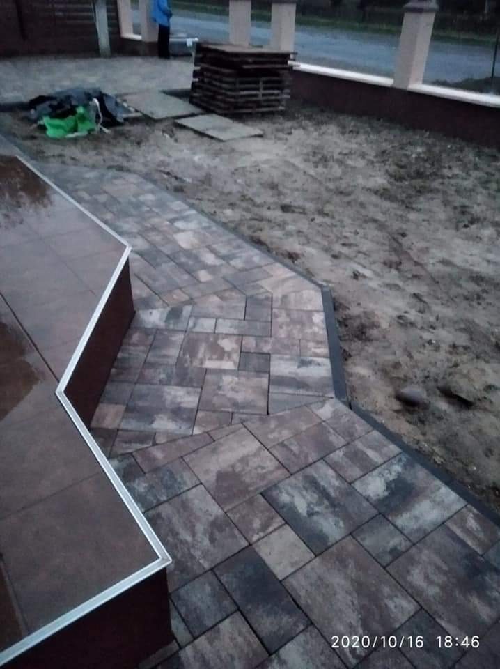 Ułożona ścieżka z kostki brukowej w odcieniach szarości i brązu, z widocznymi paletami kostki i przygotowanym podłożem w tle.