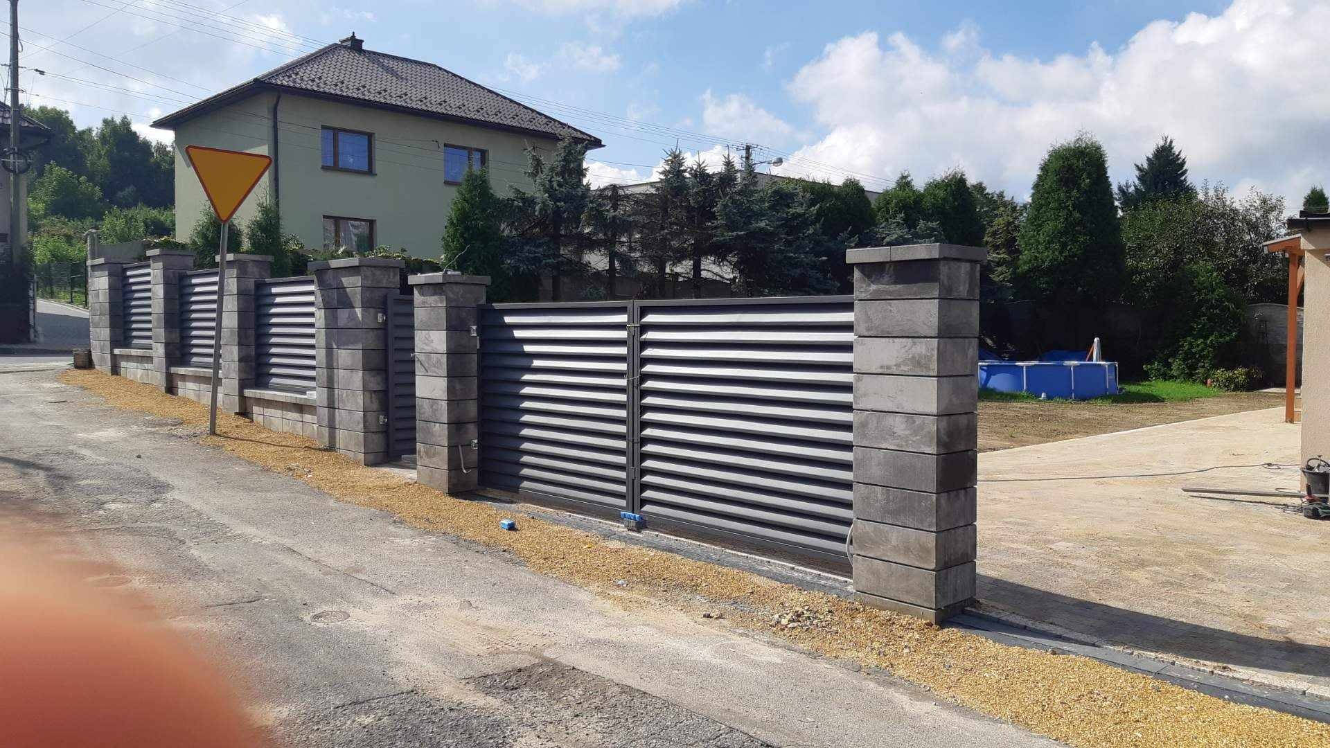 Nowoczesna brama wjazdowa przesuwna z poziomymi panelami, osadzona między betonowymi słupkami, widoczna z ulicy przed domem z basenem w tle.