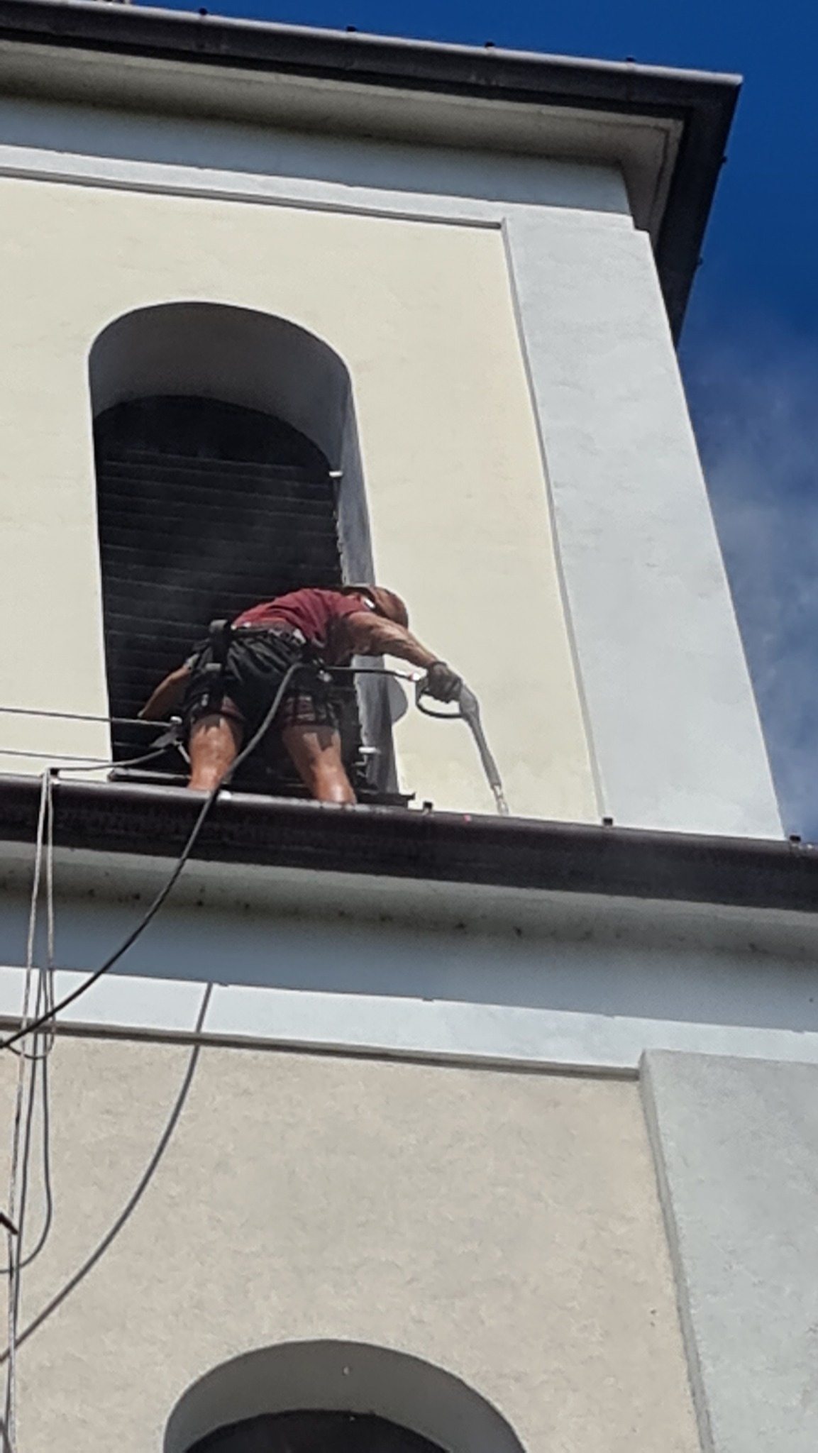 Pracownik w uprzęży, z bliska, czyści rynnę kościoła za pomocą myjki ciśnieniowej, widok z dołu