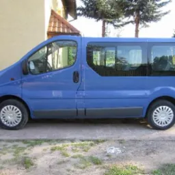 Niebieski van z przyciemnianymi szybami, zaparkowany przed budynkiem. Widok z boku, oświetlenie dzienne. Koła z srebrnymi felgami.