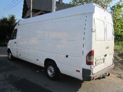 Biały furgon dostawczy, widok z tyłu i boku, zaparkowany na asfalcie, z widocznym numerem rejestracyjnym i elementami otoczenia.