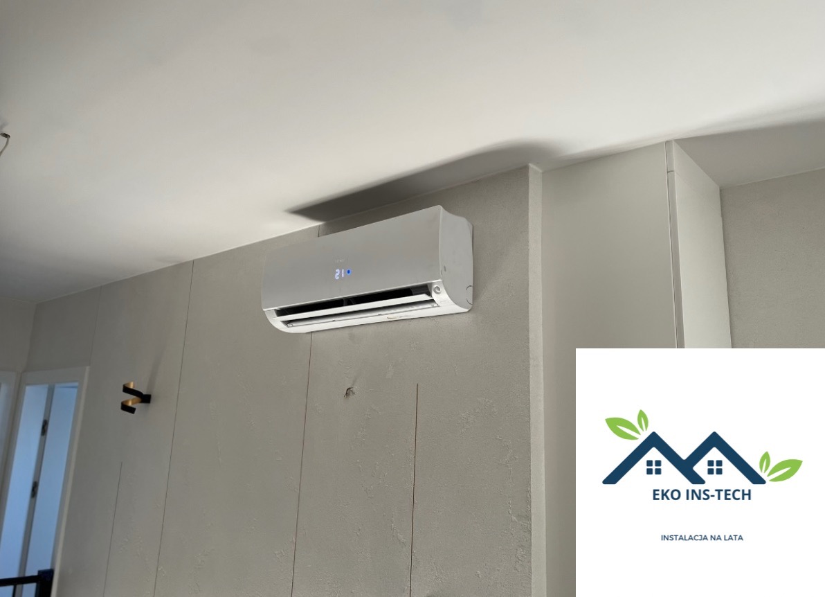 Klimatyzator ścienny z wyświetlaczem ustawionym na 21 stopni Celsjusza, zamontowany na szarej ścianie z pionowymi panelami dekoracyjnymi, widoczne logo firmy EKO INS-TECH w prawym dolnym rogu.