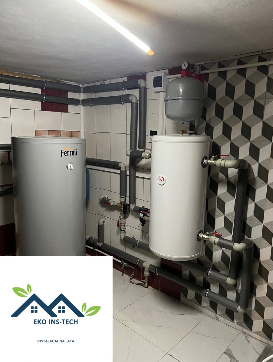 Dwa zbiorniki na wodę, jeden marki Ferolli, połączone rurami z izolacją termiczną w kotłowni z biało-czarną ścianą i logo firmy EKO INS-TECH w lewym dolnym rogu.