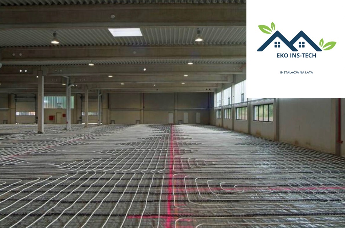 Rozległa hala przemysłowa z widoczną instalacją ogrzewania podłogowego w trakcie montażu, rurki ułożone w regularny wzór na srebrnej folii izolacyjnej, surowy betonowy strop z lampami i świetlikiem...