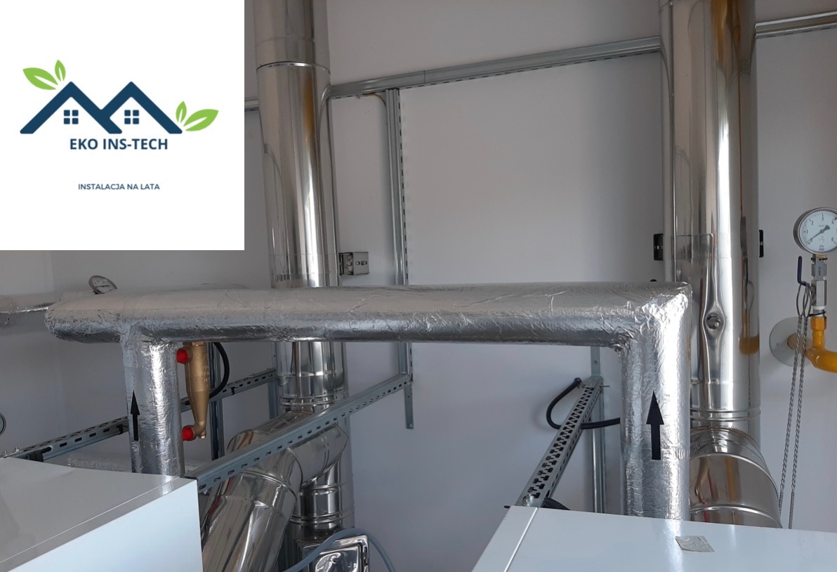Srebrne, zaizolowane rury instalacji grzewczej z widocznym manometrem, umieszczone w pomieszczeniu z białymi ścianami. Na pierwszym planie logo firmy Eko Ins-Tech.
