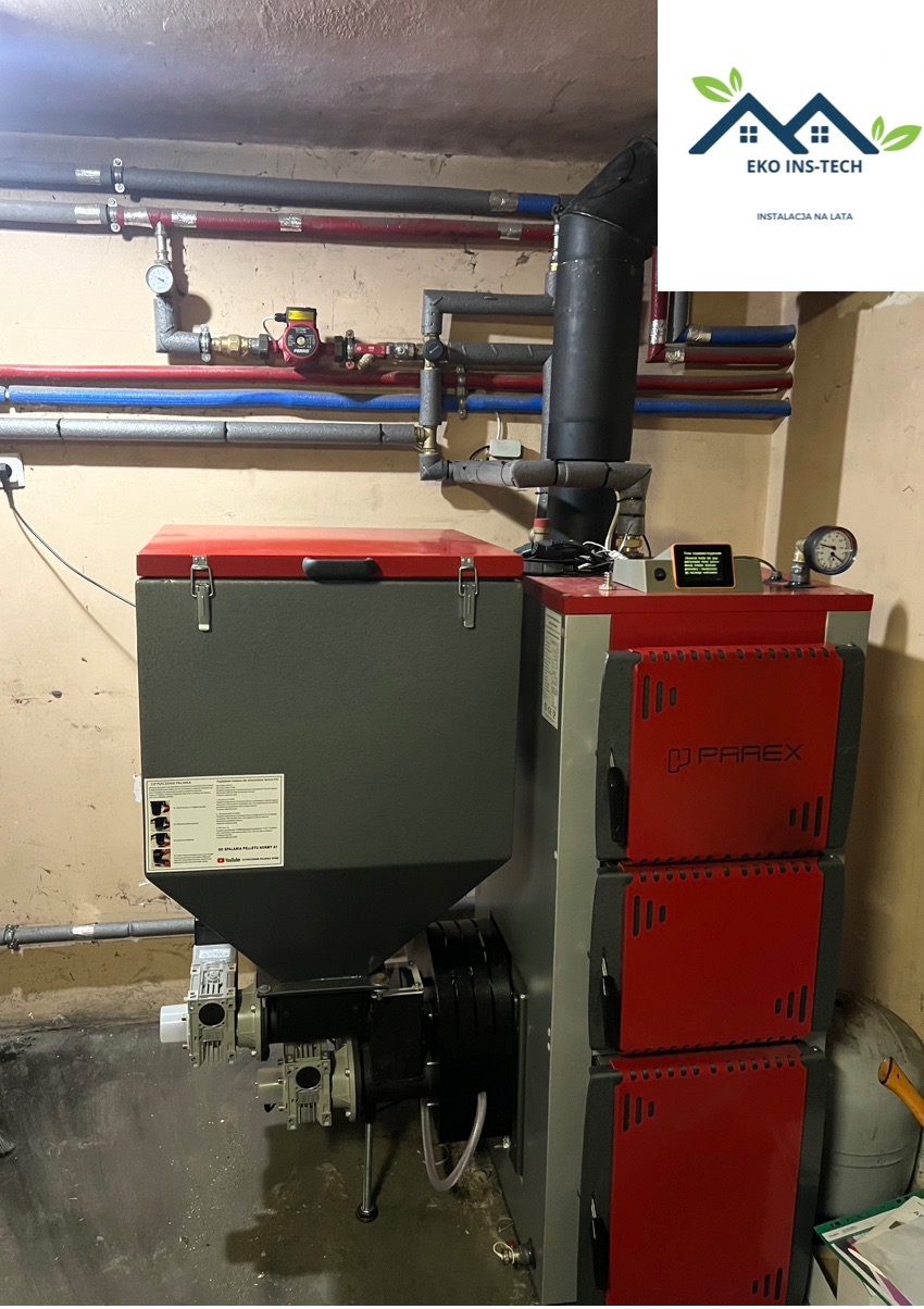 Szaro-czerwony piec na pellet marki Parex z podajnikiem, widoczne rury instalacji grzewczej, manometry i logo firmy Eko Ins-Tech w prawym górnym rogu.