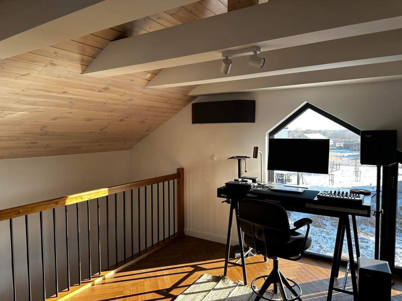 Klimatyzator ścienny w nowoczesnym pokoju na poddaszu z drewnianym sufitem, oświetlony promieniami słońca wpadającymi przez okno.