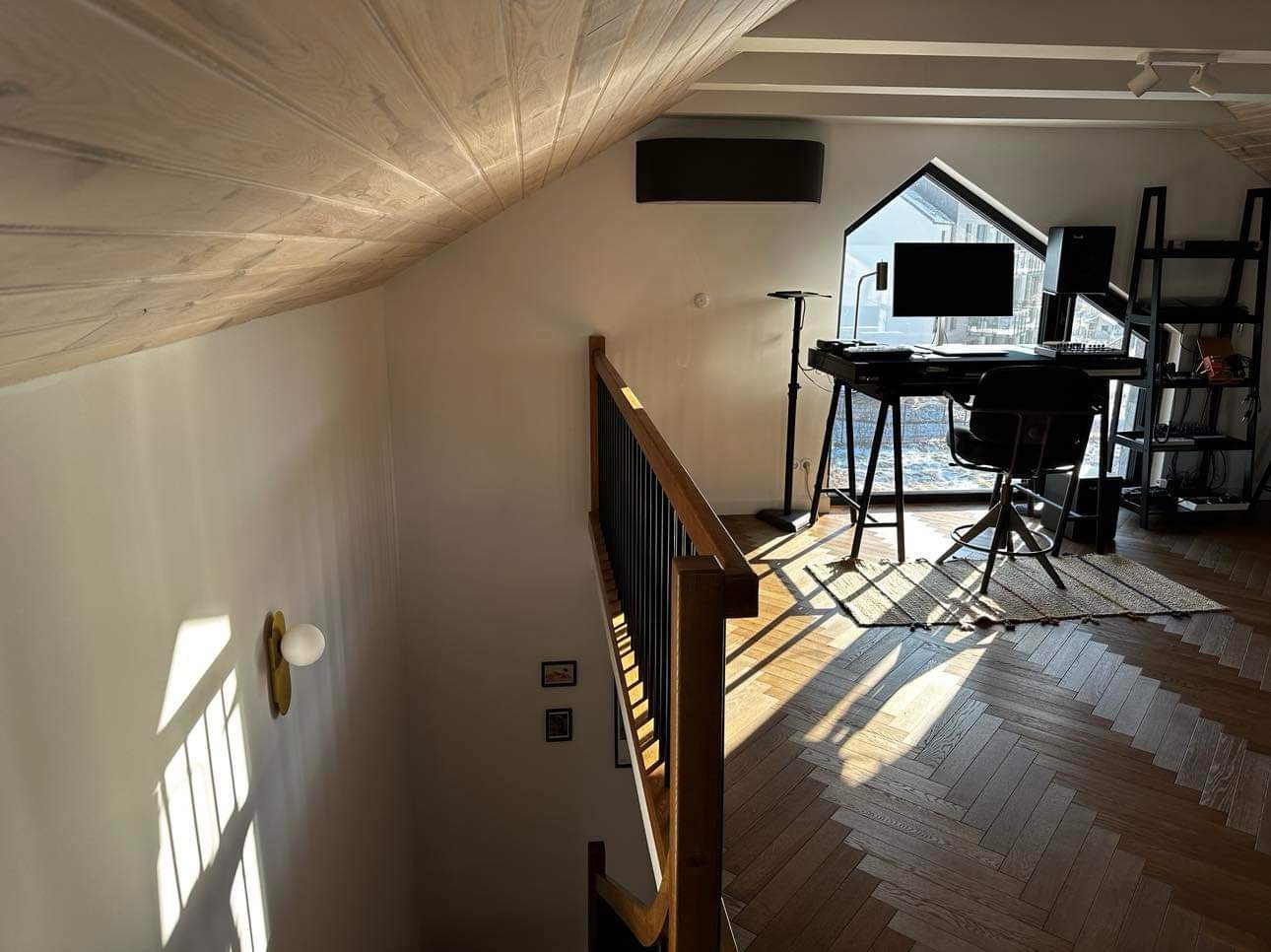 Poddasze zaadaptowane na biuro z klimatyzatorem na ścianie, widok z góry na schody, parkiet w jodełkę i okno z widokiem na zewnątrz.