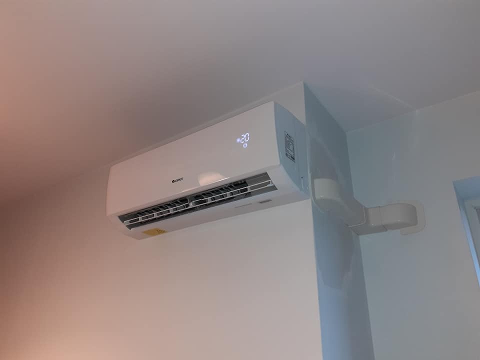 Biała jednostka klimatyzacji marki Gree zamontowana na ścianie w pomieszczeniu, widoczne rury odprowadzające.