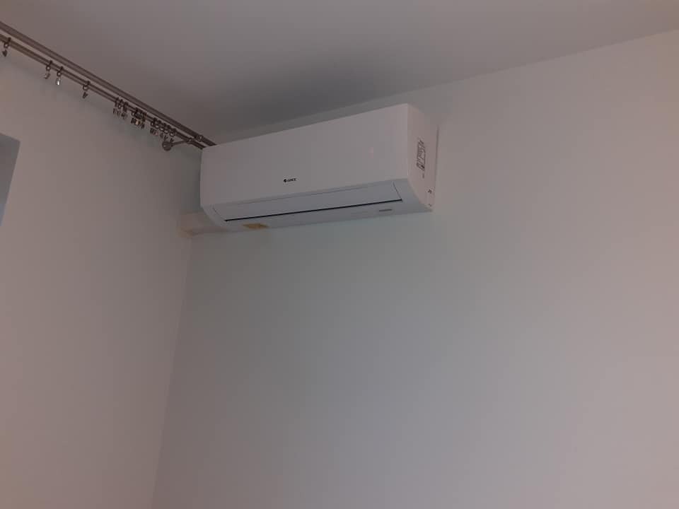 Biała jednostka wewnętrzna klimatyzacji marki Gree zamontowana na ścianie w pomieszczeniu z karniszem na zasłony