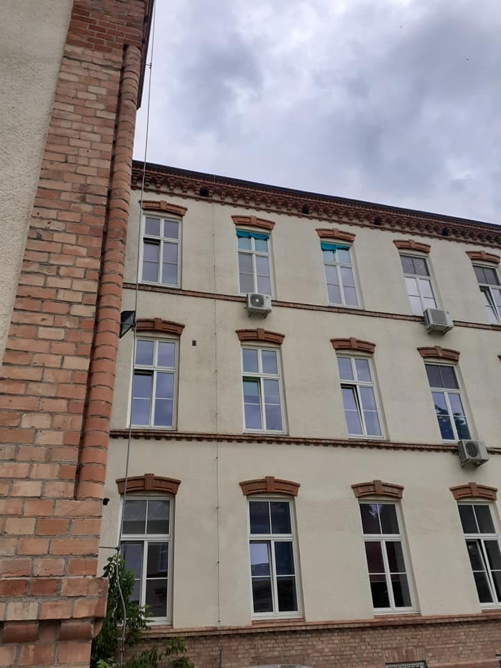 Elewacja budynku wielorodzinnego z zamontowanymi jednostkami zewnętrznymi klimatyzacji pod oknami, widok z dołu na kilka pięter.