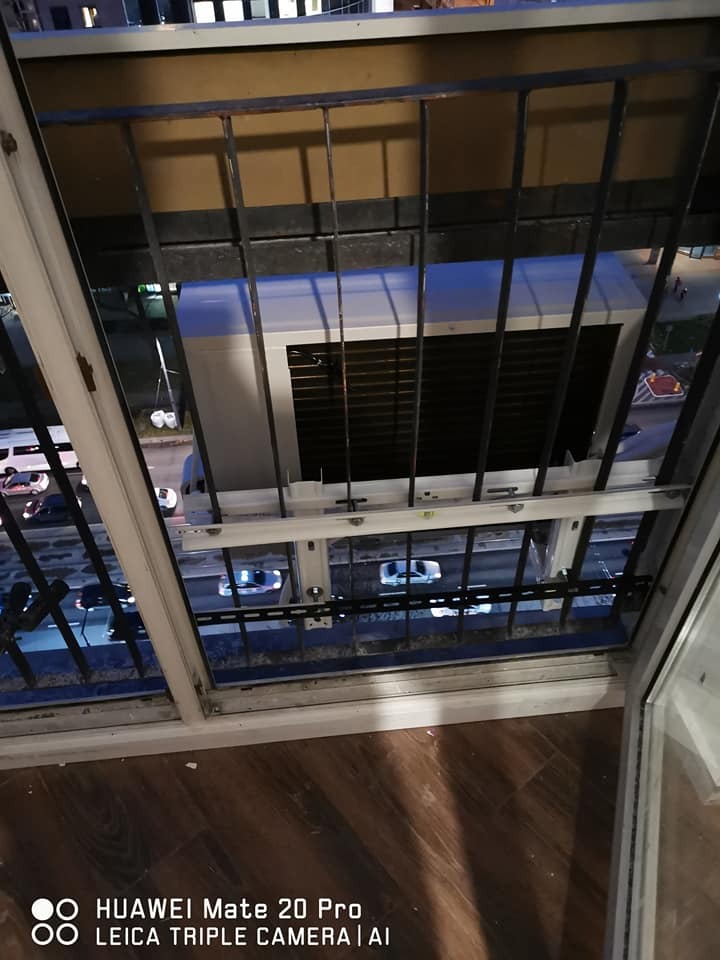 Klimatyzator okienny zamontowany na balkonie mieszkania z widokiem na nocną ulicę.