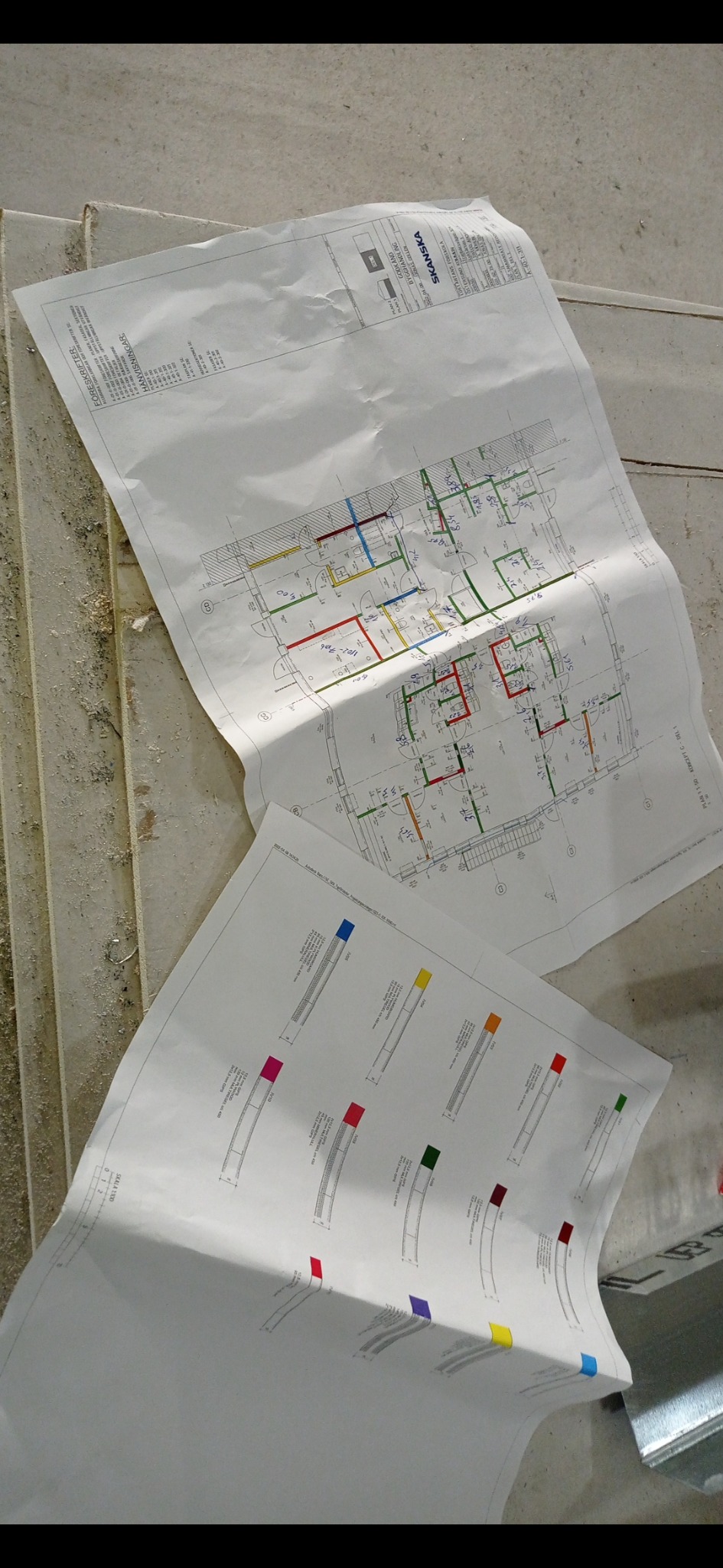 Dwa plany architektoniczne z kolorowymi oznaczeniami instalacji, leżące na surowym podłożu budowlanym, częściowo na schodach.