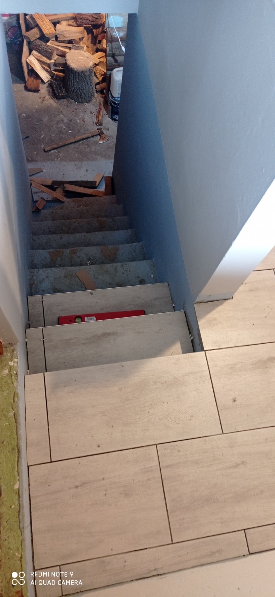 Schody w trakcie wykańczania, pokryte płytkami imitującymi drewno, poziomica na jednym ze stopni, widoczne przygotowania do dalszych prac.