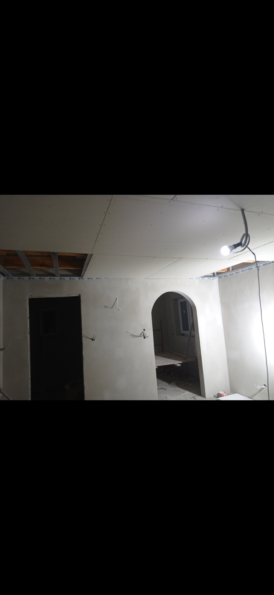Wnętrze w trakcie remontu, widoczne ściany z gładzią, otwór drzwiowy i łukowe przejście, sufit z płyt gipsowo-kartonowych z widoczną konstrukcją, przewody elektryczne wystające ze ścian.