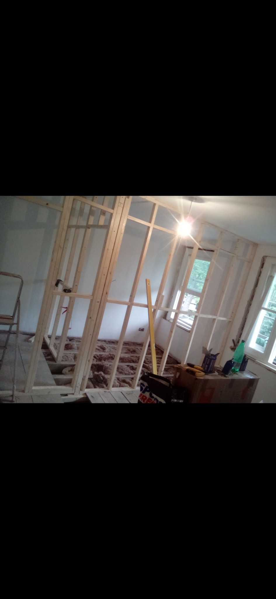 Konstrukcja szkieletowa ścian działowych z drewna, widoczna izolacja podłogi, poziomica oparta o ramę, okno w tle.