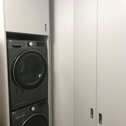 Morti Joanna Sieńkowska - Szara pralka i suszarka LG umieszczone jedna na drugiej w białej szafie wnękowej z minimalistycznymi uchwytami.