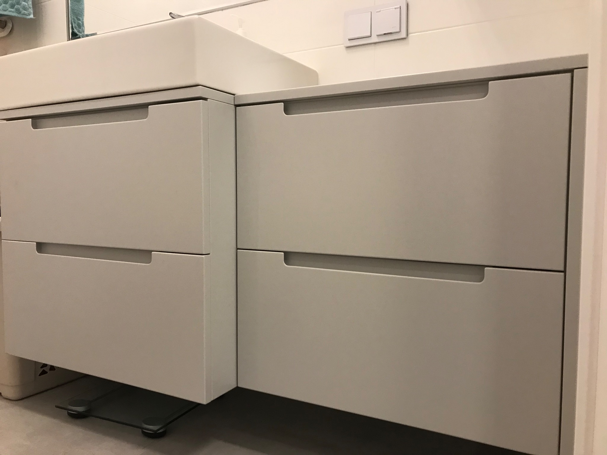 Szare szafki łazienkowe z umywalką i wbudowanymi uchwytami, widoczne waga łazienkowa na podłodze.