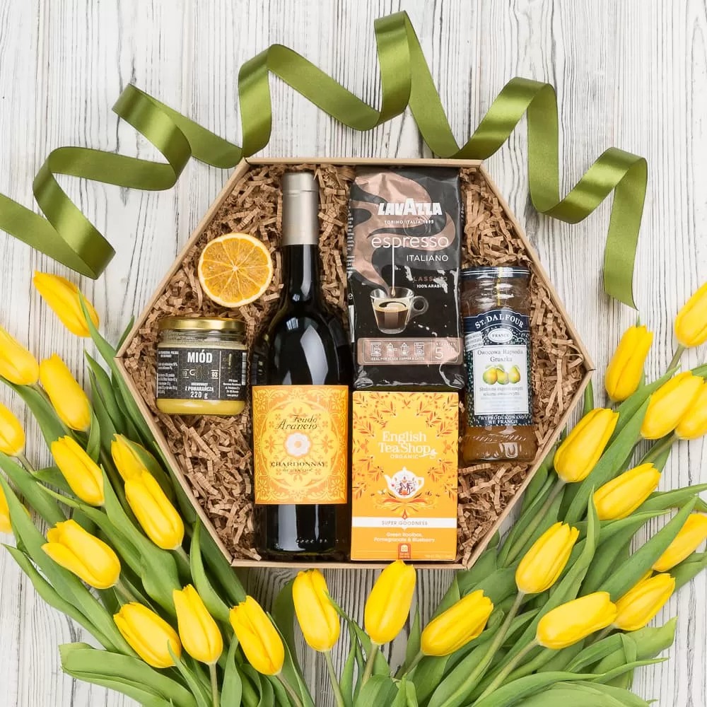 Elegancki prezentowy zestaw w heksagonalnym pudełku z wypełnieniem z papierowych wiórków, zawierający butelkę wina Chardonnay, słoik miodu pomarańczowego, kawę espresso, herbatę English Tea Shop...