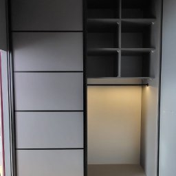 RAF-ART - Szara szafa wnękowa z przesuwnymi drzwiami i oświetleniem LED wewnątrz, widoczne półki i drążek na ubrania, na podłodze panele imitujące drewno.