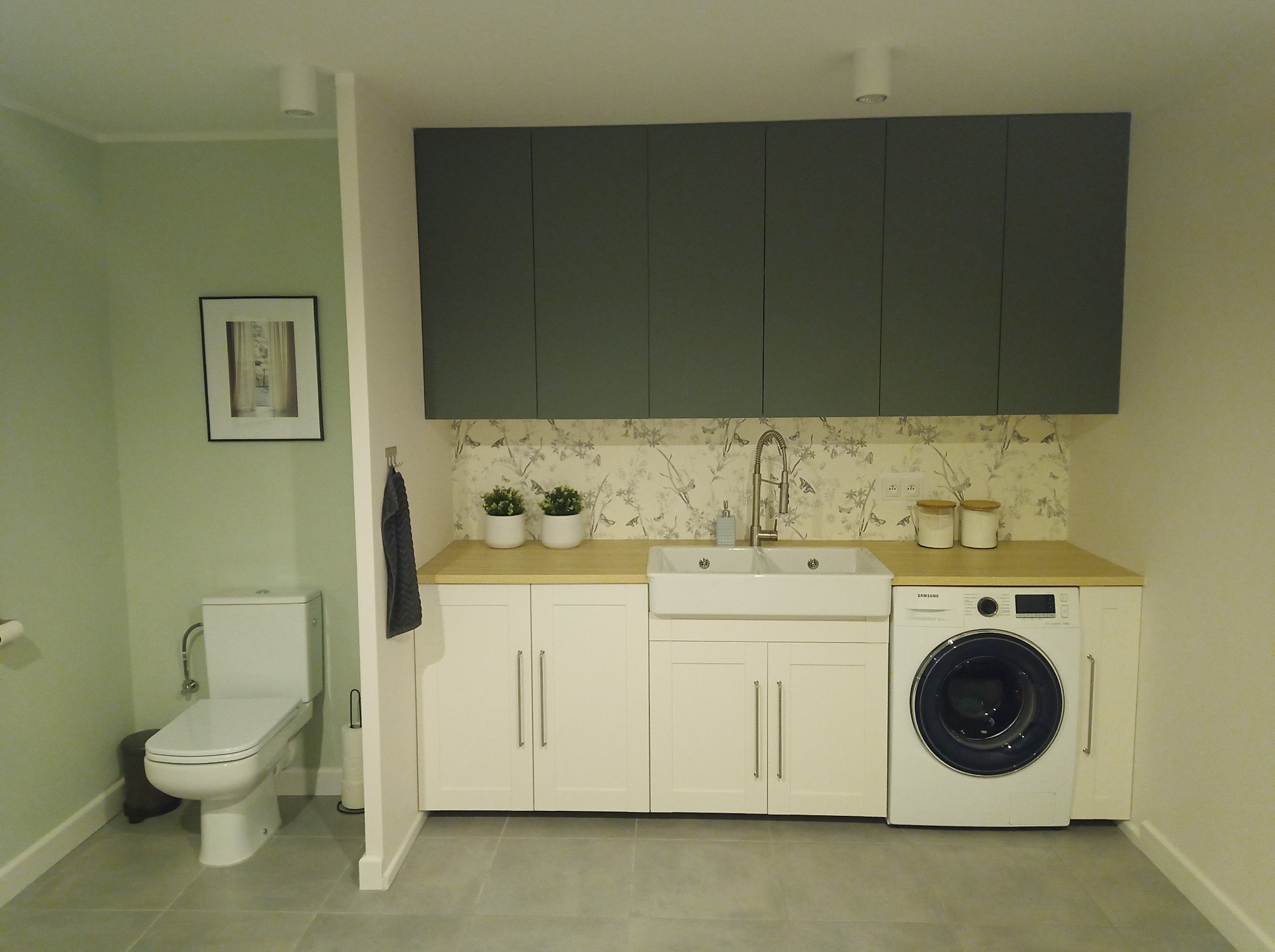 Funkcjonalna aranżacja łazienki w Częstochowie z toaletą, umywalką wpuszczaną w blat, pralką i szafkami wiszącymi w kolorze ciemnej zieleni.