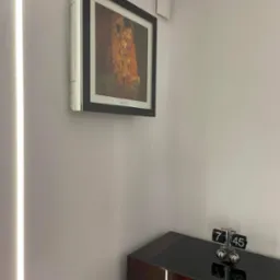 Nowoczesny klimatyzator ścienny z funkcją wyświetlania obrazu, prezentujący reprodukcję 'Pocałunku' Gustava Klimta, zamontowany w minimalistycznym wnętrzu nad błyszczącą komodą z zegarem przerzutowym.