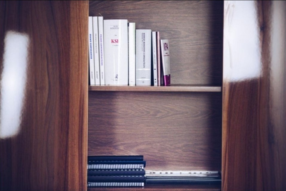 Półka z książkami prawniczymi i notatnikami w drewnianym regale, oświetlona z boku.