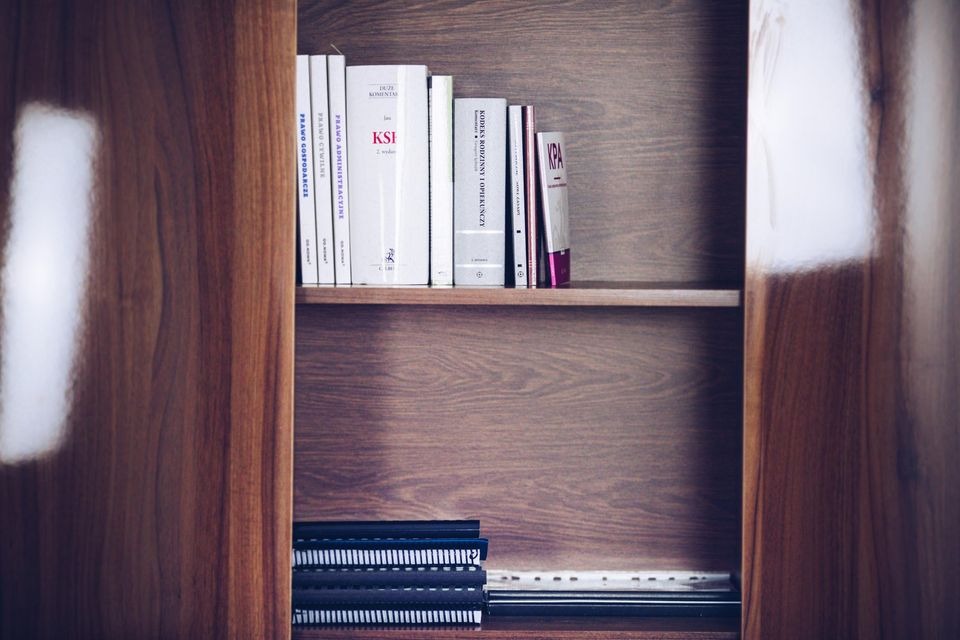 Półka z książkami prawniczymi, w tym Kodeks Rodzinny i Opiekuńczy oraz Prawo Gospodarcze, na drewnianej półce w biurze.
