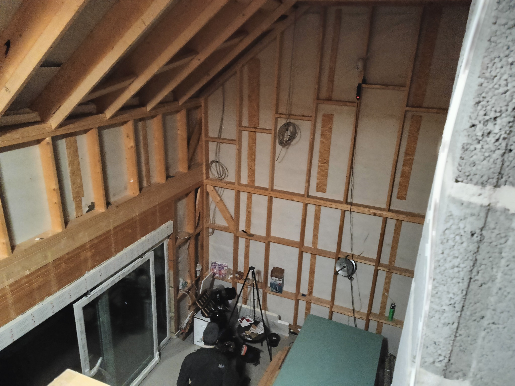 Wnętrze poddasza w trakcie adaptacji: drewniana konstrukcja szkieletowa, izolacja między elementami, widoczne przewody elektryczne, okna dachowe i materiały budowlane na podłodze.