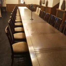 Długi, drewniany stół z krzesłami w klasycznym stylu, ustawiony w eleganckim wnętrzu z wysokimi sufitami i dekoracyjnymi elementami.