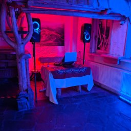Michał Ostrowski GASTROOSTRY - DJ setup z laptopem i głośnikami JBL oświetlony czerwonym i niebieskim światłem w rustykalnym wnętrzu.
