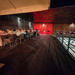 Michał Ostrowski GASTROOSTRY - Uroczysta kolacja firmowa na drewnianym tarasie, oświetlona czerwonymi światłami, z muzyką na żywo w tle.