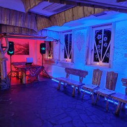 Michał Ostrowski GASTROOSTRY - Rustykalne wnętrze z drewnianymi elementami oświetlone czerwonym i niebieskim światłem, z nagłośnieniem i laptopem na stole.