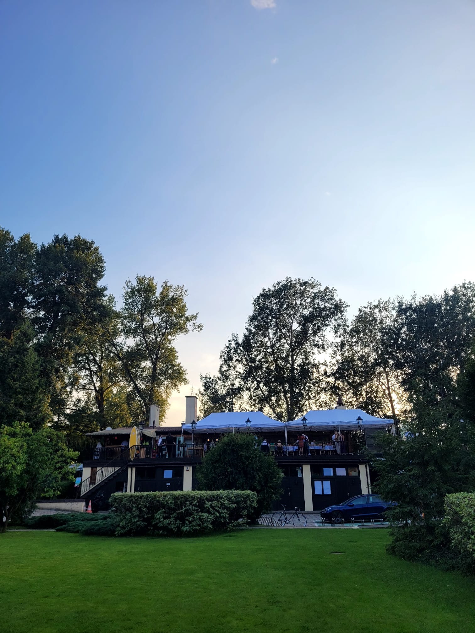 Restauracja z tarasem na dachu, widok z zewnątrz, zieleń dookoła, błękitne niebo w tle.